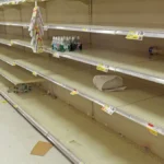 Close-up of empty cream-colored grocery store metal shelving units with pricing tags attached.